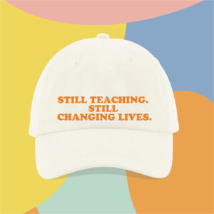 White baseball cap with orange text reading "Still teaching. Still changing lives." set against a colorful, abstract background.
