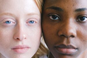 Close-up of two women resting their faces together, one with light skin and blue eyes and the other with dark skin.