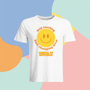 White T-shirt featuring a large yellow smiley face and orange text that reads 'Still teaching, changing lives' on a bright, abstract background.