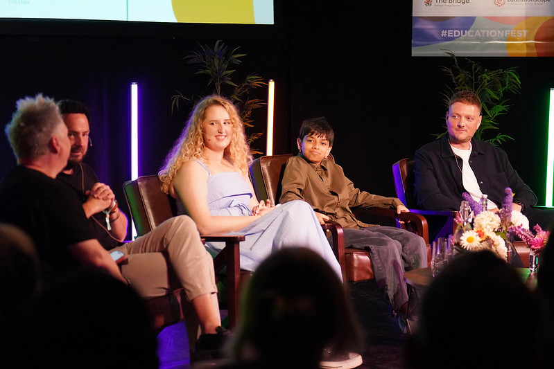 Panel of five people seated on a stage in a discussion, with colorful backlights and a banner reading #EducationFest behind them.