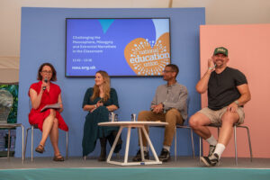 Panel discussion with four speakers on a blue stage; a woman in red speaks into a microphone, others listen, with a large screen showing the National Education Union and session title in the background.
