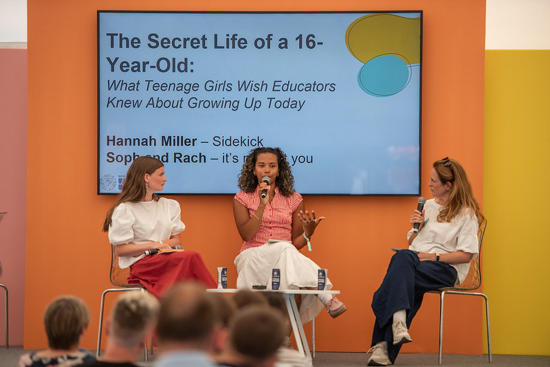 Panel discussion with three women on a stage in front of a large screen showing 'The Secret Life of a 16-Year-Old...' subtitle.